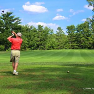 Golfer in a red shirt taking swing on golf course